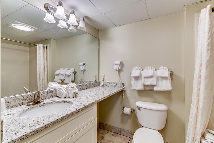 A bathroom with a granite countertop sink, toilet, and mirror