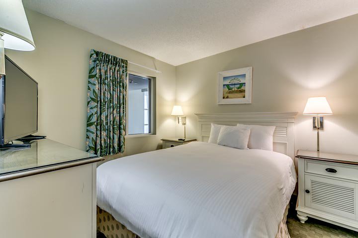 A hotel room with a bed, nightstands, a TV, and a window.