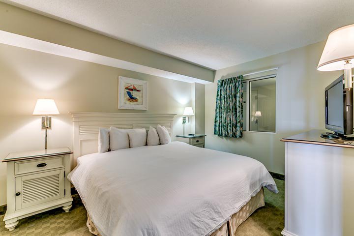 A wide view of a hotel room with a large bed, two nightstands, a TV, and a dresser.
