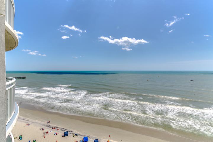 A beach view from a balcony with the ocean and sky in the background.