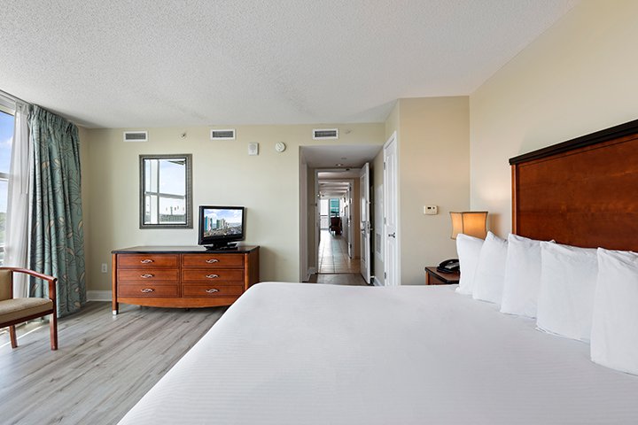 A hotel room with a large bed, dresser, TV, chair, and lamp.