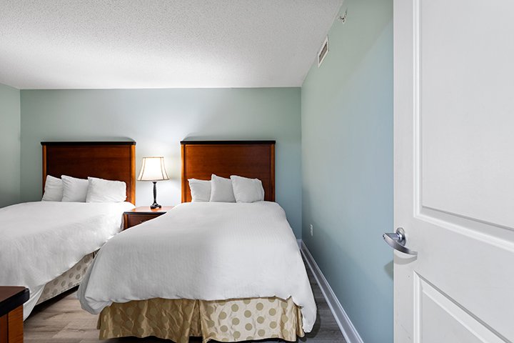 A hotel room with two beds, wooden headboards, and white bedding.