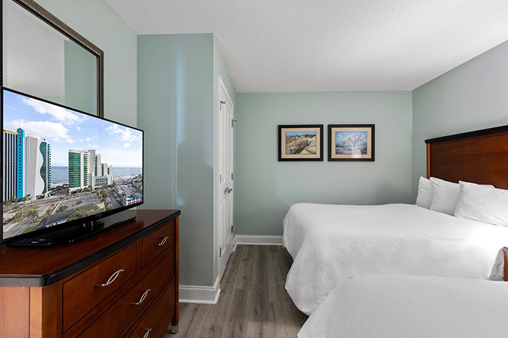 A wide view of a hotel room with two beds, a TV on a dresser, and light green walls.