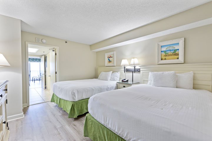 A hotel room with two beds, a nightstand, and an open doorway leading to a balcony.