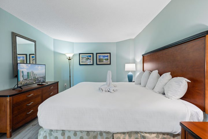 A hotel room with a large bed, dresser, TV, and lamp.