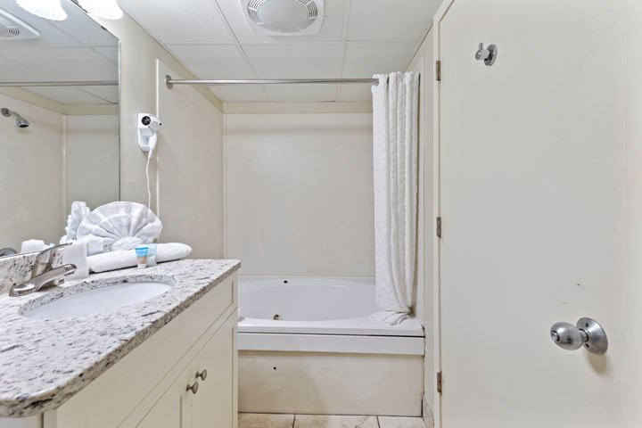 A bathroom with a granite countertop, a sink, a mirror, a bathtub with a shower curtain, and a cabinet.