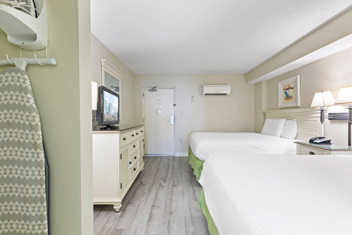 A hotel room with two beds, a dresser, TV, and lamp.