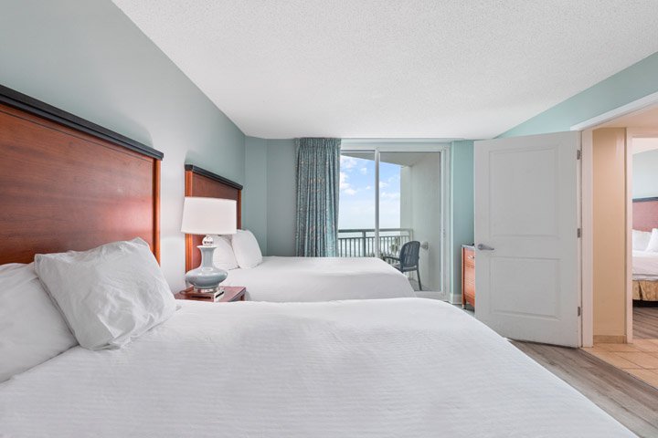 A hotel room with two beds, a nightstand, and a balcony