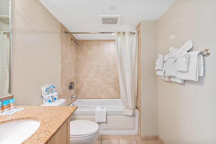 a clean bathroom with a granite countertop, tiled shower, toilet, and bathtub
