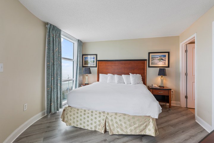 A hotel room with a large bed, two nightstands with lamps, and a window with a view.