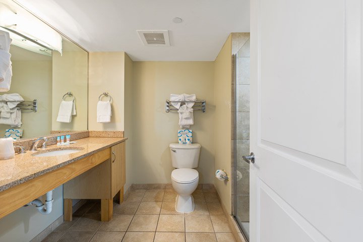 A standard hotel bathroom with a granite countertop, tiled floor, and glass-enclosed shower.