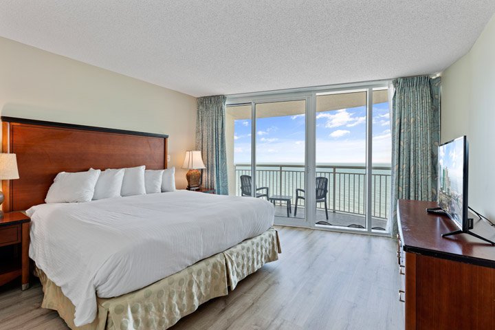 A wide view of a hotel room with a large bed, balcony, and TV.
