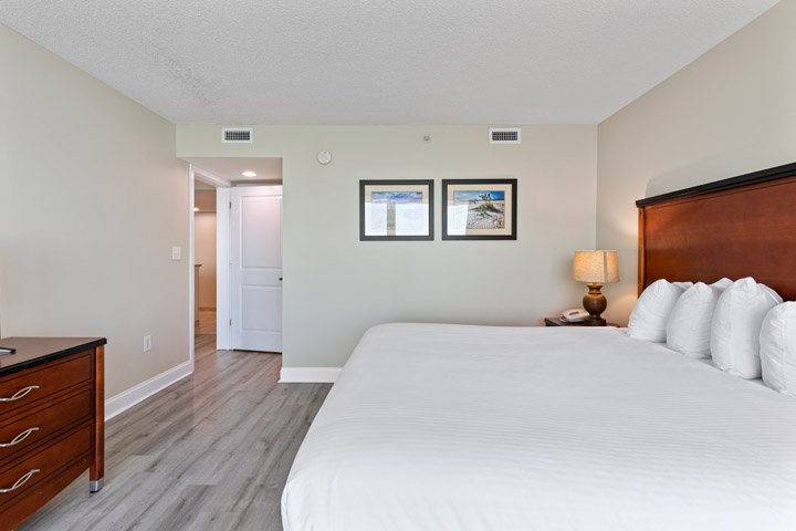 A wide view of a hotel room with a large bed, dresser, and artwork on the wall.