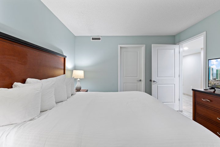 A wide view of a bedroom with a large bed, dresser, and TV.