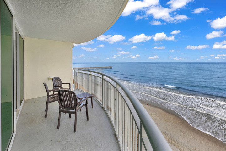 A balcony with a table and chairs overlooking the ocean.