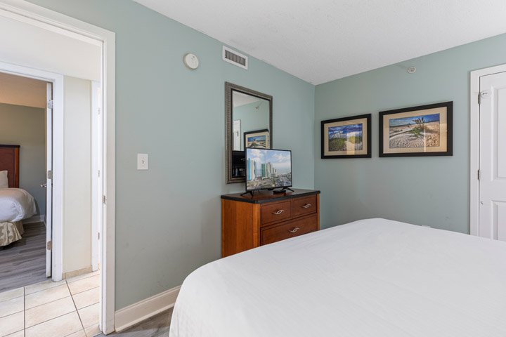 A hotel room with a large bed, dresser, and TV