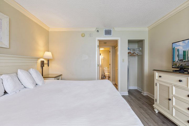 A hotel room with a large bed, TV, closet, and bathroom doorway.