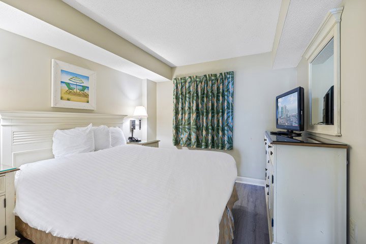 A hotel room with a large bed, TV, dresser, and mirror.
